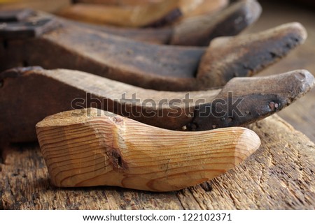 Simple wooden shoe lasts (molds) in a row at old working bench. Closeup, daylight