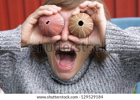 Young woman making fun, holding sea urchin shells in front of her face like two big eyeballs