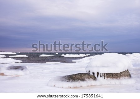 Stones under ice layer, ice-free sea at background. Focus on stones in the front