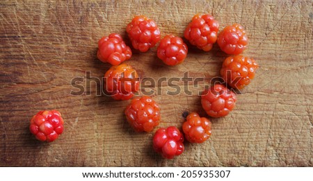 Cloudberries (Rubus chamaemorus) arranged in heart form on wooden cutting board. Closeup, daylight.