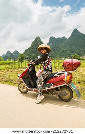 Yangshuo Vicinities . Woman travels around the Yulong River Valley on the electro - scooter.