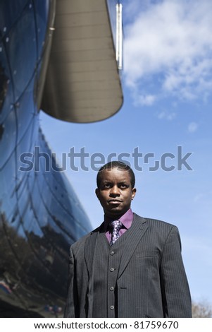 Black business man outdoor in front of modern building. Blue sky. Grey suit with violet chemise