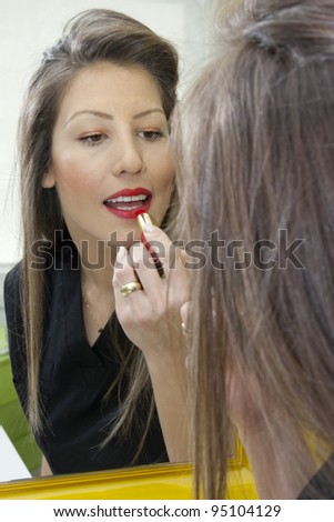 Beautiful lady applying make up in the mirror