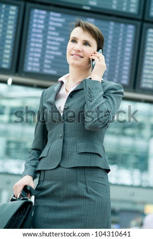 Portrait of smiling business woman on mobile phone in front of panel at airport