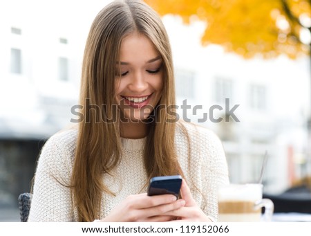 Young Beauty Woman Writing Message On Cell Phone In A Street Cafe. Looking Down