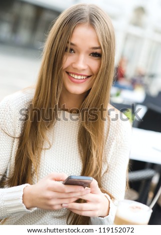 Young beauty woman writing message on cell phone in a street cafe. Looking at camera