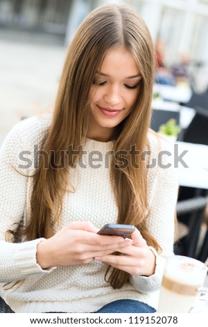 Young beauty woman writing message on cell phone in a street cafe. Looking down