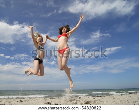 Mother and daughter jumping on the beach. Summer vacations