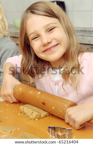 Little girl holding the rolling-pin ans smiling in the camera