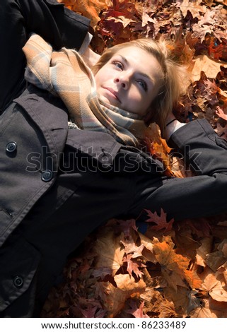 Young beautiful woman lying in yellow leafs in autumn ant thinking about