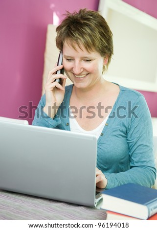 Portrait of happy middle age woman with phone and computer working at home