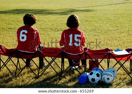 A pair of soccer players watch from the bench.