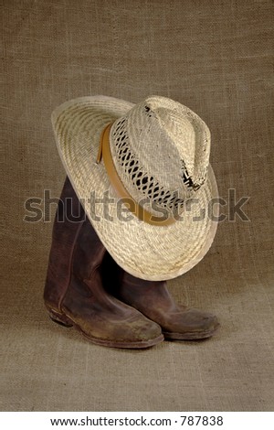 Muddy cowboy boots and straw hat on a burlap background.
