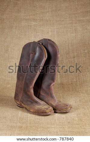 Muddy cowboy boots on burlap background.