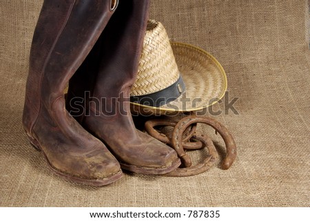 Muddy cowboy boots, straw hat and old horseshoes on a burlap background.