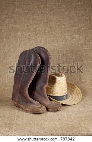 Muddy cowboy boots and straw hat on a burlap background.