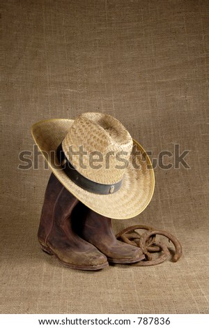 Muddy cowboy boots, straw  hat and old horseshoes on a burlap background.