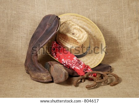 Muddy cowboy boots, straw hat , bandanna and old horseshoes on a burlap background.