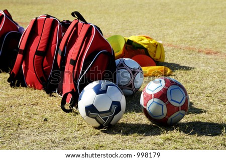 Soccer balls and bags on the sidelines at a youth soccer game.