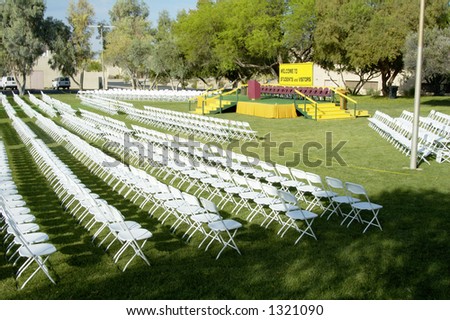 Folding chairs and stage set up for an outdoor college graduation ceremony.