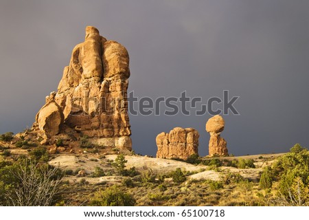 The sun breaks out over Arches National Park after a rainstorm passes over. Dark clouds and the Balanced Rock formation are seen in the background.