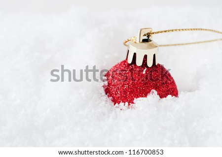 A sparkly red glitter Christmas bauble, with gold clasp and gilt string, sunk into fake white snow to the right of frame.  Snow provides copy space to left.