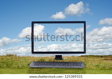 Composite image of a cloud computing concept.  Monitor and keyboard facing front and positioned on grass with blue sky and white fluffy clouds in the background.  Clouds pass across the screen.