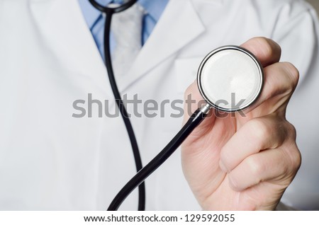 Close up of a Doctor\'s hand, holding a stethoscope outstretched towards the viewer.  Doctor\'s white coat provides space to the left side of frame.
