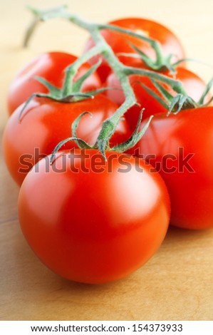Close up of six ripe red salad tomatoes with four still attached to vine and resting on wood laminate table.  Shot just above eye level with main focus on tomato in foreground.