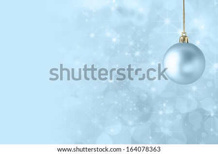 A pale blue Christmas bauble, suspended on gold string against a star filled twinkly bokeh background, fading into solid colour to provide copy space on the left side.