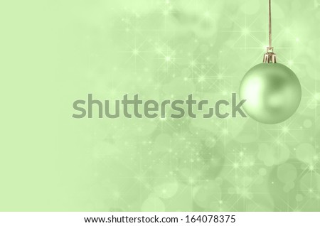 A green Christmas bauble, suspended on gold string against a star filled twinkly bokeh background, fading into solid colour to provide copy space on the left side.