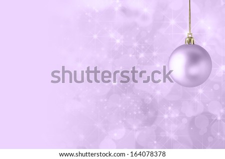 A lilac purple Christmas bauble, suspended on gold string against a star filled twinkly bokeh background, fading into solid colour to provide copy space on the left side.