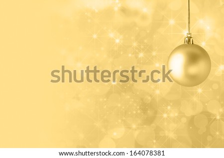 A golden yellow Christmas bauble, suspended on gold string against a star filled twinkly bokeh background, fading into solid colour to provide copy space on the left side.