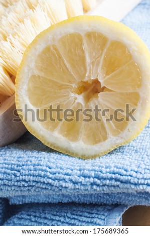 Close up of half a lemon, facing front, piled together with a wooden bristle scrubbing brush and a microfibre cloth to represent natural, non-toxic cleaning.