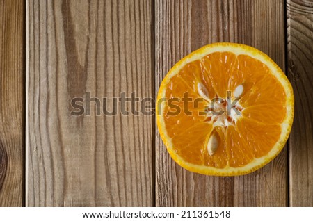 Overhead shot of an orange half with cut side facing upwards, flesh and pips exposed.  Set on right side of frame on a wood planked surface that has been slightly desaturated for a grungy effect.