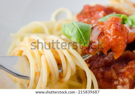 A bowl of spaghetti pasta, tomato sauce and basil leaf with cheese, with close-up of raised fork in foreground, wrapped in spaghetti and dipped in sauce.