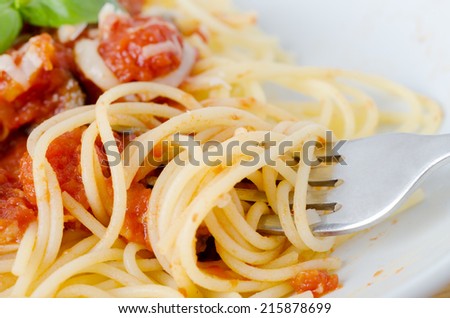 A bowl of  pasta, tomato sauce and basil leaves with cheese. Close-up of fork winding and raising spaghetti in foreground.