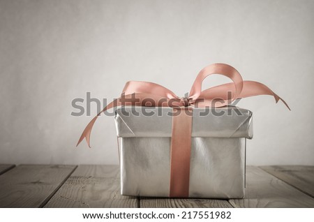 A gift box with closed lid, wrapped in silver paper and tied to a bow with a satin ribbon.  Placed on a weathered old wooden table with copy space behind and above.