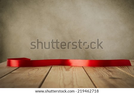 A red satin ribbon, curved and facing front to provide copy space for message, placed on a wood plank table against parchment background.  Vintage style.