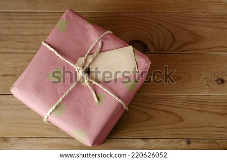Overhead shot of a wrapped pink paper parcel with heart pattern, tied with string.  Blank label faces upwards to provide copy space.  Set on an old, worn wooden table.