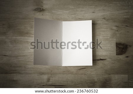 Overhead shot of a blank greeting card, lying face upwards and opened on a wooden planked table.  Low saturation and vignetted vintage style.