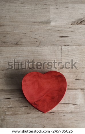 Overhead shot of a red  heart shaped wooden box, painted with suedette texture on an old wood planked table.  Love or Valentines Day concept.