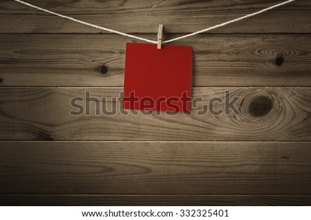 One individual square of festive red note paper, pegged to a string washing line.  Wood plank background.  Low saturation and vignette gives a retro or vintage feel.