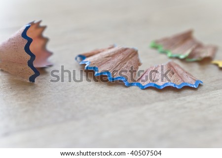 Macro (close-up) of coloured wooden shavings from sharpened art pencils, scattered on a birch table in natural daylight.