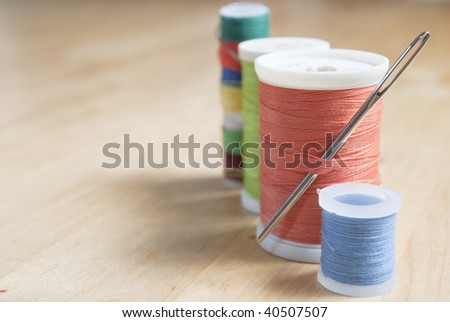 Close up of a row of cotton reels with inserted needle in a diagonal row on a wooden birch table.