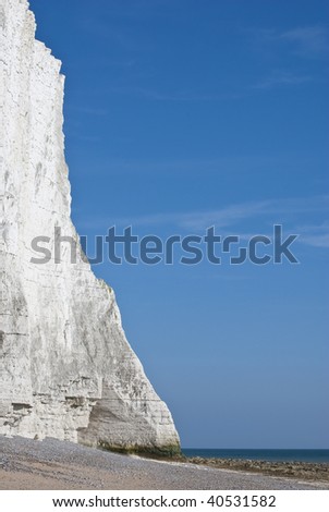 Portrait shot of a white chalk cliff at the sea\'s edge.  Sand, sea and blue sky visible.   Copy space.