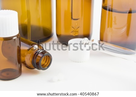 A collection of amber glass bottles (spray, dropper and pill) and pillules used in homeopathic pharmacy.
