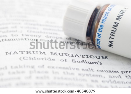 A closeup shot of a homeopathic materia medica opened on the page for Nat Mur. A bottle of Nat Mur pills (6th potency) rests on the opened book.