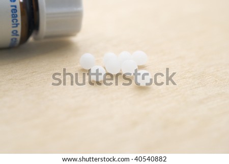 A closeup of homeopathic pills resting on a light wooden surface with a closed pill bottle partly in-frame to the upper left (background).  Macro shot, shallow depth of field.