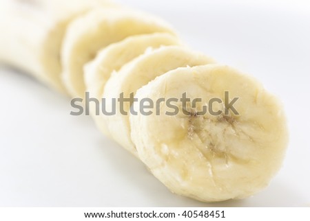 Close-up of sliced banana seated diagonally across frame with white background on either side.  Main portion in soft focus in the background.